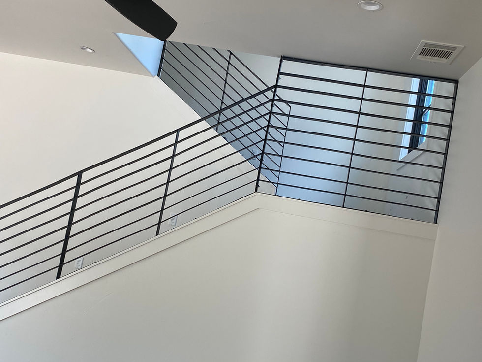 A modern indoor staircase with custom railing in black metal and white walls, ascending to an upper floor where a window lets natural light fill the space—an elegant touch in residential construction.