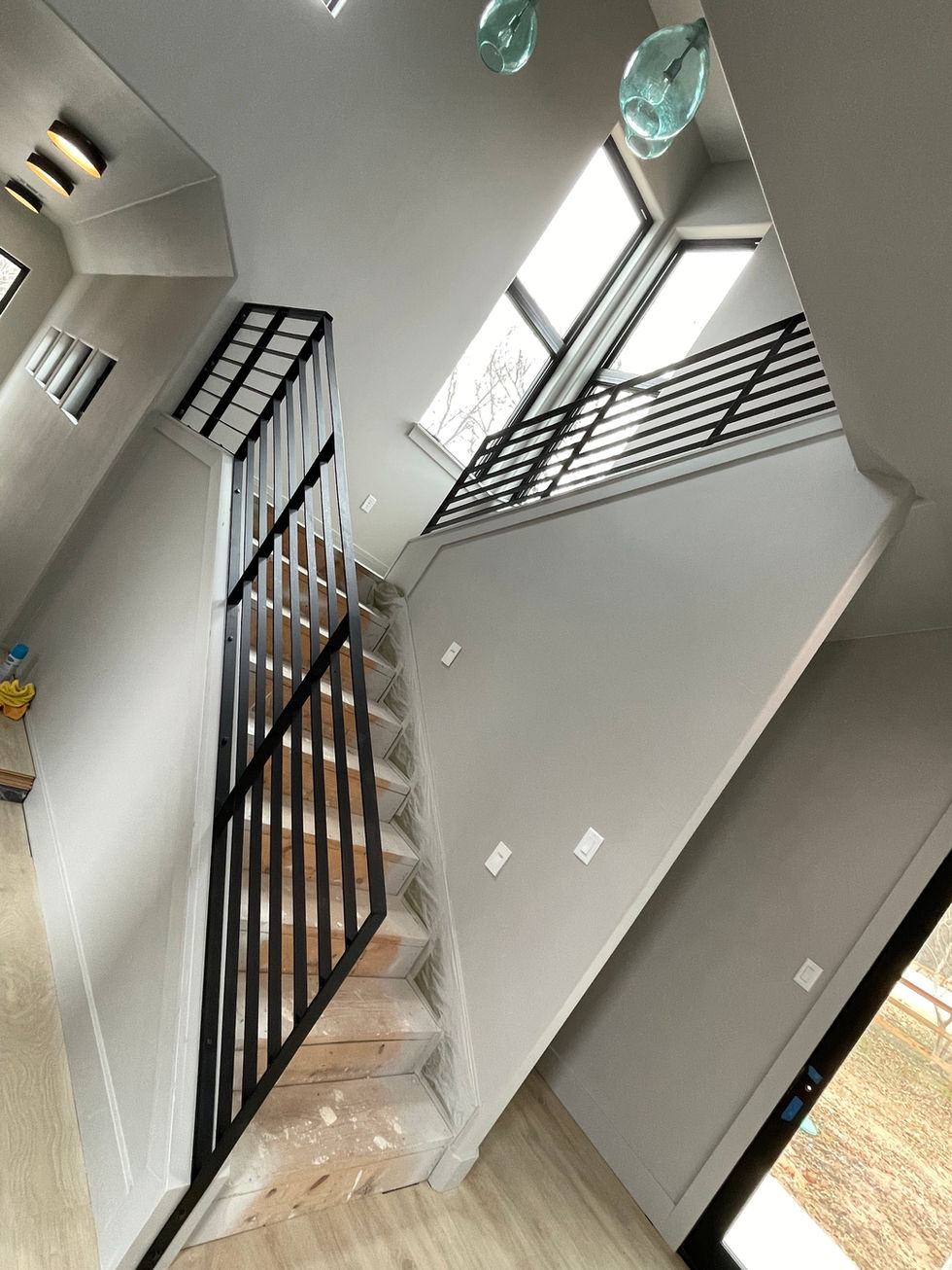 Modern indoor staircase with custom railing in black metal, light wood steps, and unfinished treads. Large windows fill the space with natural light, while blue glass pendant lights accent this residential construction.