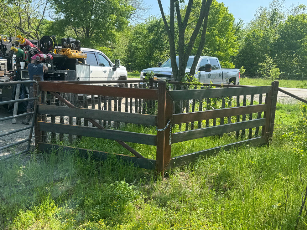 A metal trash can enclosure sits on grassy ground with a chain on the gate. Behind it is a parked white Chevrolet truck and trees with green foliage, suggesting recent mobile welding work in the area.