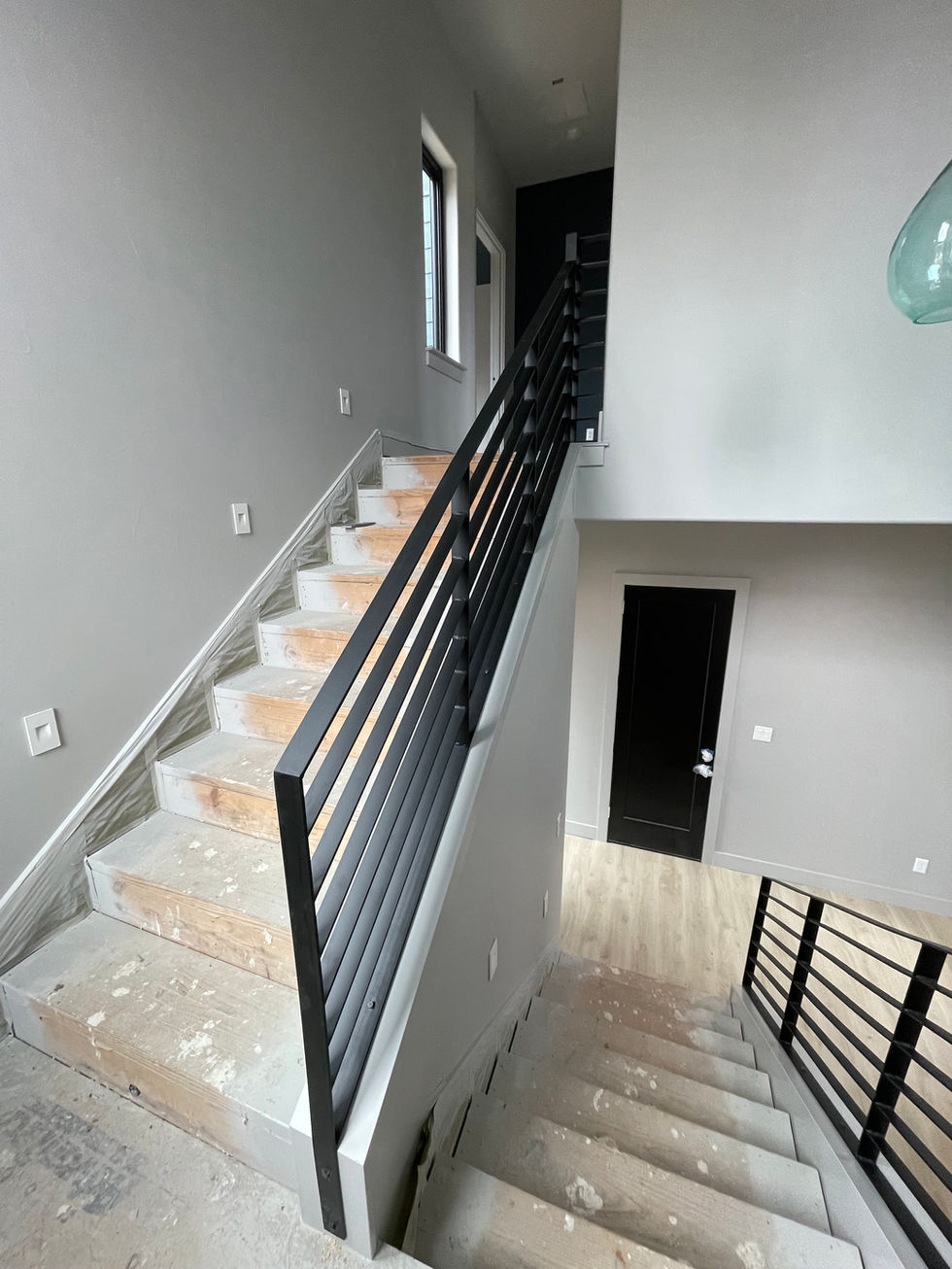 A modern indoor staircase with unfinished wooden steps, a custom railing of black metal, and light gray walls highlights residential construction in a house under renovation. Natural light streams in through a window on the staircase landing.