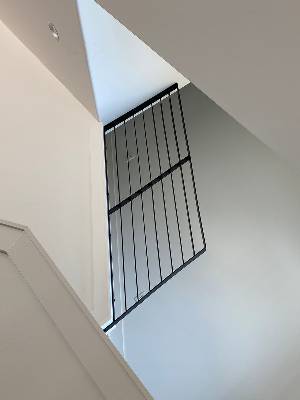 A view looking up a staircase, featuring a custom railing in black metal against white and light gray walls, with strong geometric lines and natural light from above—a showcase of refined residential construction.