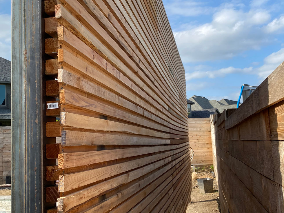 A close-up side view of a newly constructed wooden fence with horizontal slats, adjacent to another wooden privacy wall, under a partly cloudy sky in a residential area.