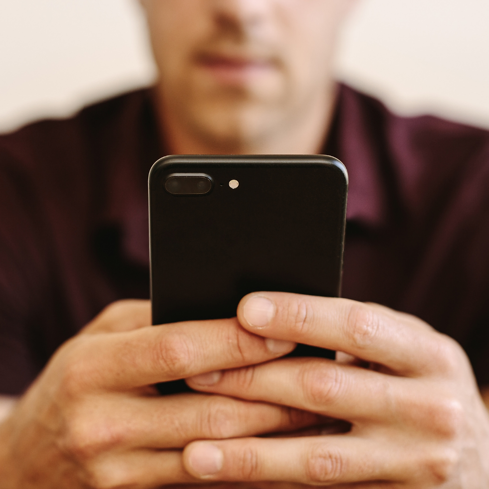 Blurred man in maroon shirt holds a black smartphone close to the camera indoors.