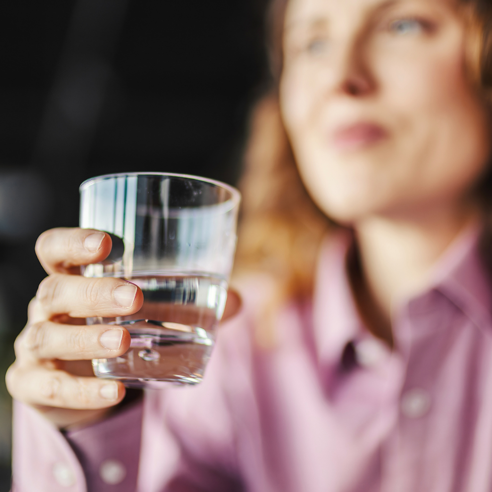 Close-up of a woman in a pink shirt holding a glass of water, with a blurred face against a dark background.