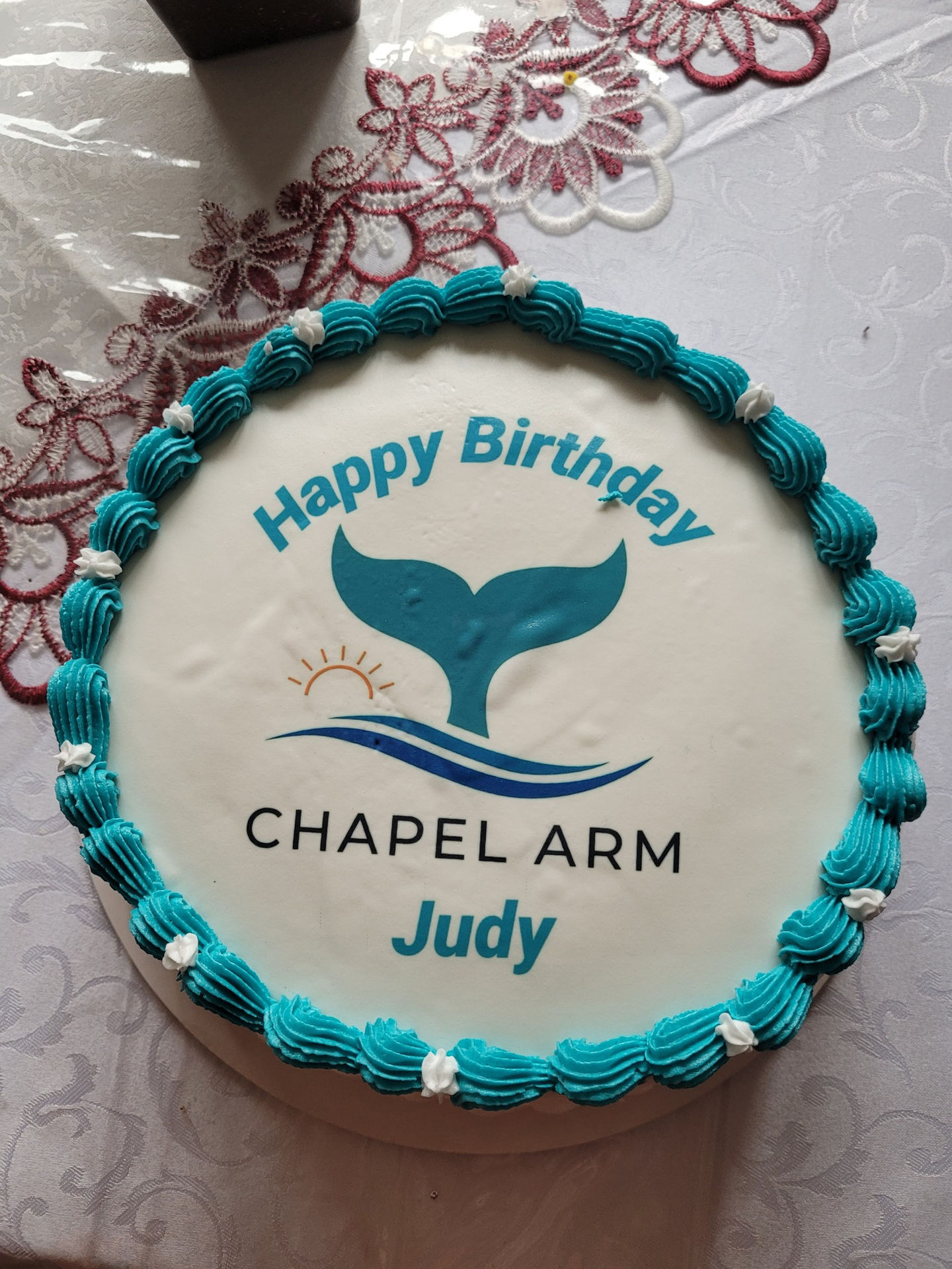 A top down view of a birthday cake that reads "Happy Birthday Judy" around the Chapel Arm whale tail logo.