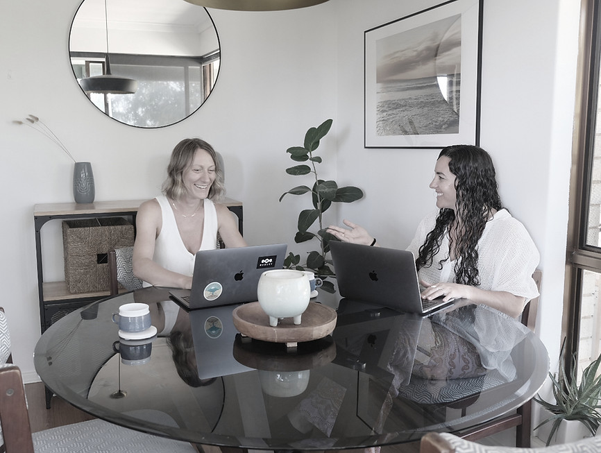 Two women working on laptops at a table, discussing work together ABOUT Startup Digital