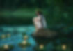 Slavic girl sits on stone on shore lake. Nymph fantasy woman hugs knees. Long black hair.