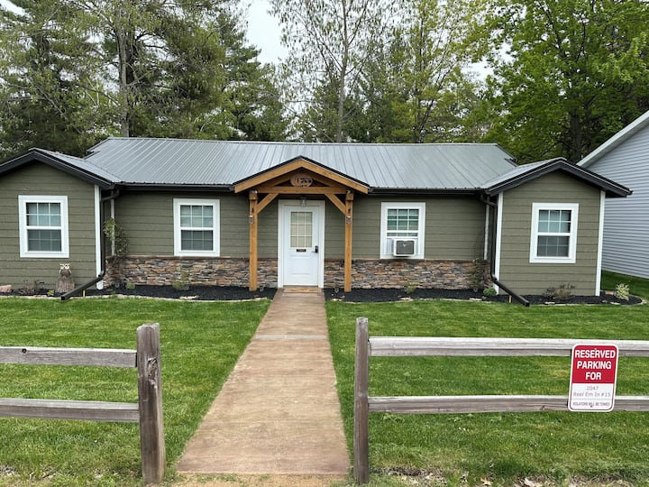 Green cabin with a timber porch and a split-rail fence