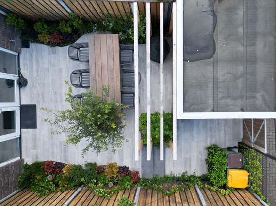 Vogelvlucht van moderne stadstuin met lange houten eettafel, pergola en groene borders.