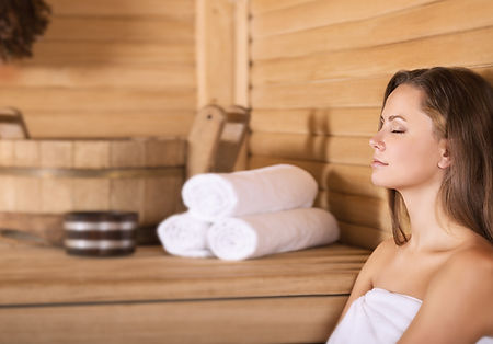 Woman lookin relaxed in sauna with eyes closed towels and bucket are placed behind her