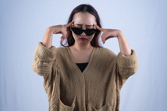 Young Asian woman in sunglasses touching temples with headache on white studio backdrop.jp