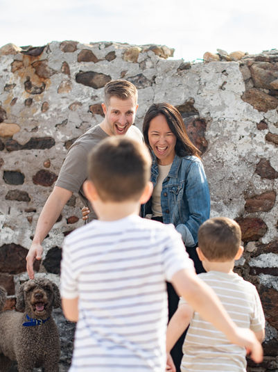 Two children run towards their laughing parents and dog.