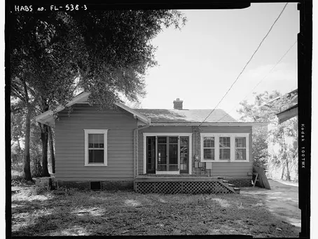 Black and white photo of a small single-story starter home with wood siding, front steps, and a screened porch representing modest first time buyer housing.