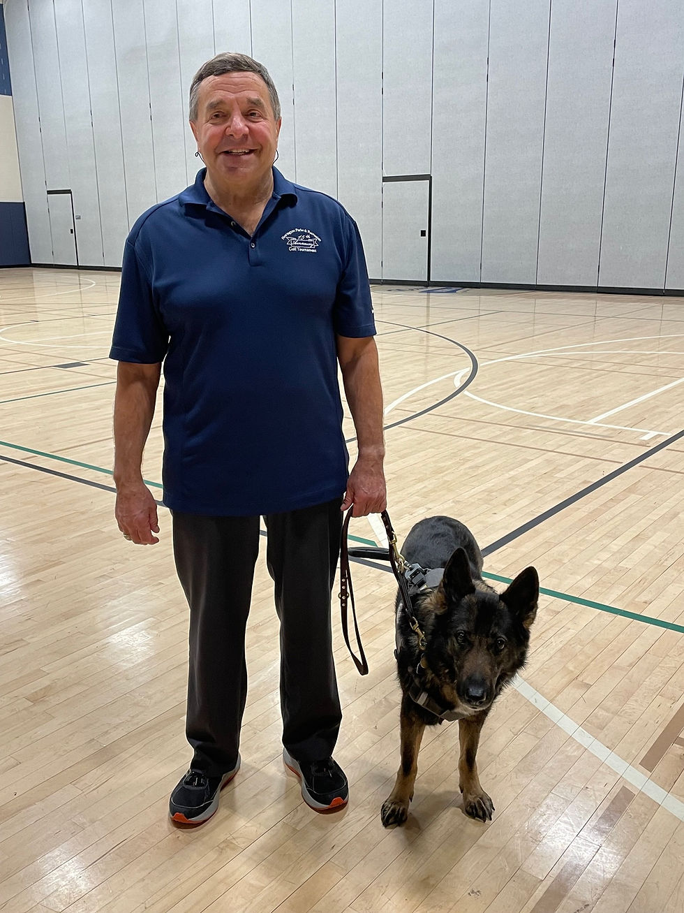 Bill DeMaio recently retired after 47 years of public service. He stands in the gym of the Mortensen Community Center with his guide dog Lyric. (photo by Mark Jahne)