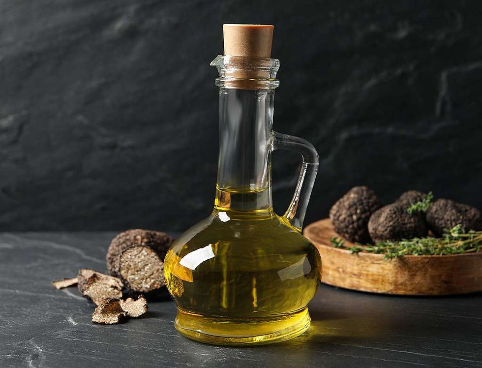 Glass bottle of oil with cork stopper on a dark stone surface, surrounded by sliced and whole truffles on a wooden plate.