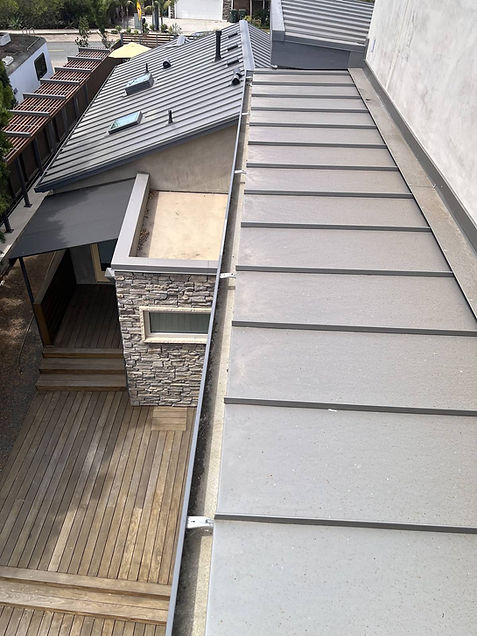 Clean gutter along a standing-seam metal roof above a wood deck after gutter cleaning