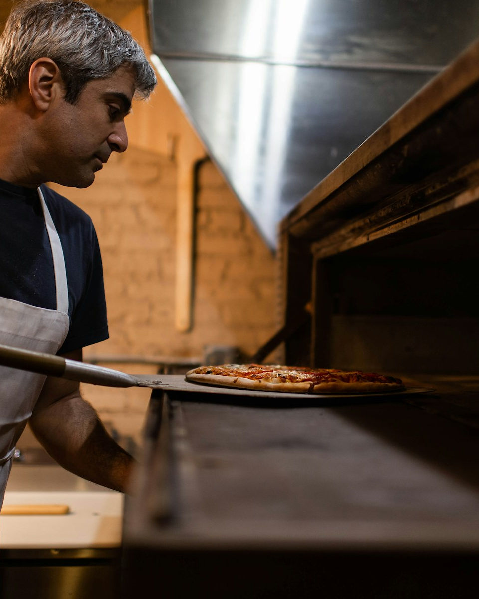A pizzeria owner sliding a pizza into the oven