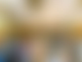 Bride and groom dance under white drapery and chandeliers in a festive hall. Guests sit at tables adorned with colorful flowers and lights.