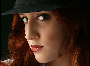 Woman with red hair and hat posing in a white shirt, looking at camera.