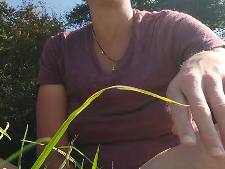 Aline Lourtie assise dans une prairie. Elle chante