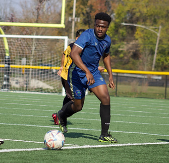 A soccer player in yellow and a soccer player in blue going for the same ball on a soccer field