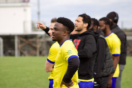 The soccer team in yellow stands on the sidelines and looks out unto the field.
