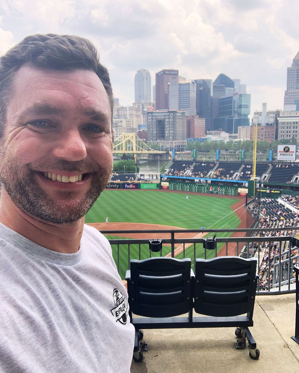 Sports Travel Tom inside PNC Park with downtown Pittsburgh visible behind the baseball field.
