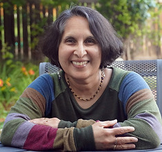Author Shuah Khan leans forward on a table with her arms in front of her.