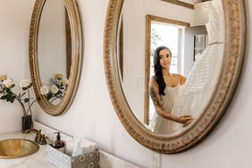 A mirror is reflecting the bride, who is looking at her reflection.