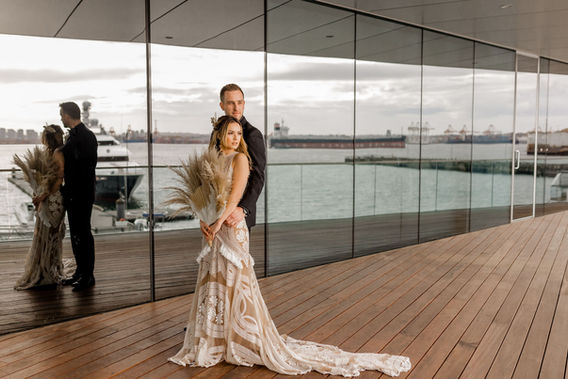 A bride and groom pose outdoors on a patio.