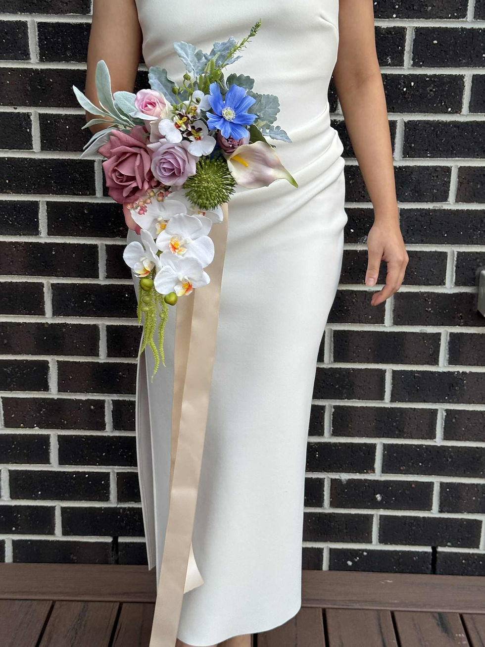 Bride in white dress holding real touch artificial bridal bouquet with white orchid, blue cosmos, dusty pale pink roses.