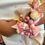 Thumbnail: Front view close up - female in white dress wearing wrist corsage featuring soft rose flower bud, pink flowers & satin ribbon