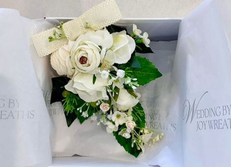 Stunning handmade white and cream dress corsage with green leaves, baby's breath, hydrangea blooms, finished with a white jute ribbon bow. Enclosed in a box with Wedding by Joy Wreaths silver embossed tissue paper.
