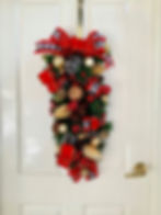 Long Christmas Wreath on white door with gold pinecone, natural pinecone, gold bauble, red ribbon, F1 black chequered ribbon