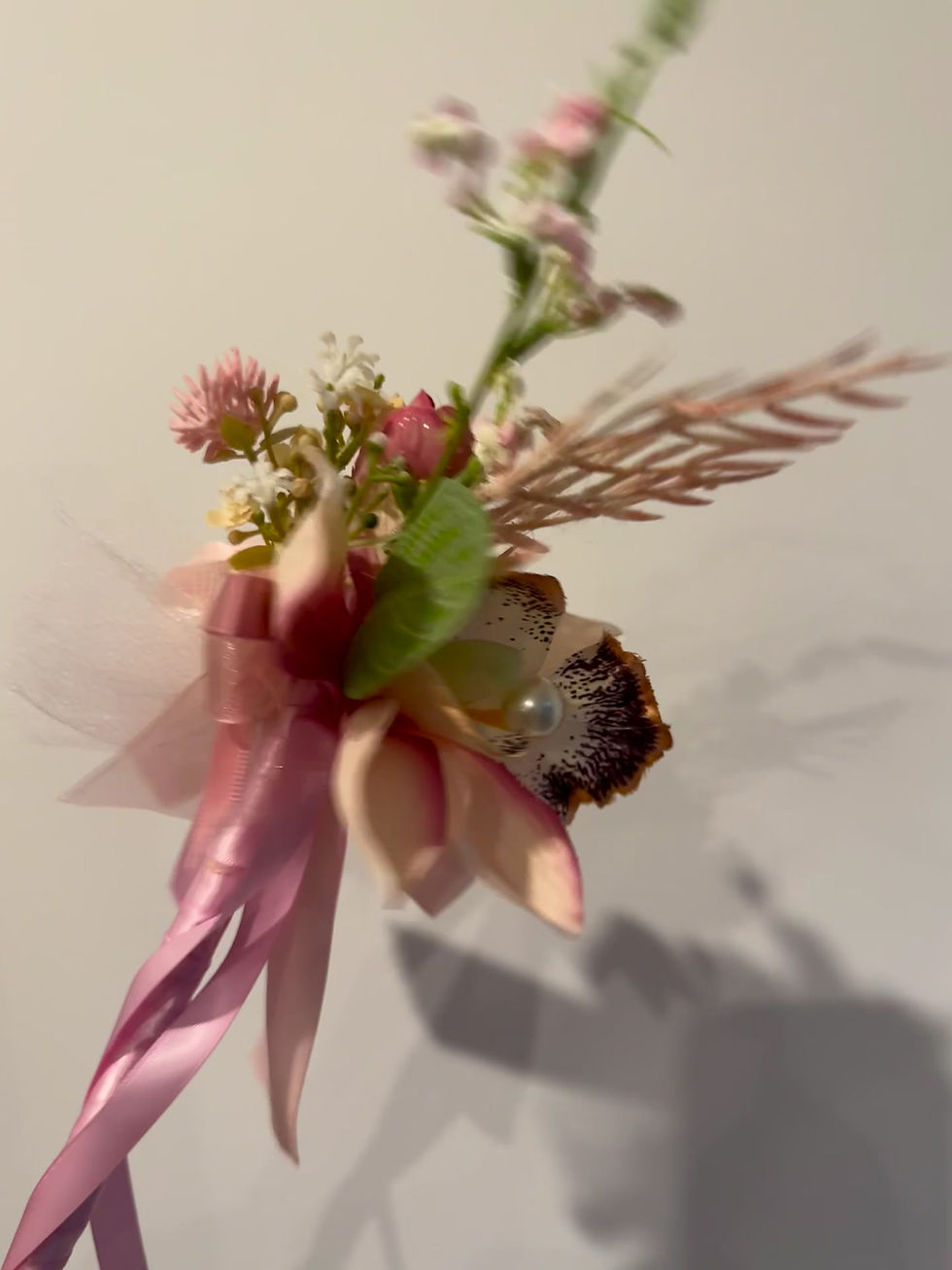 Thumbnail: Pink wedding ceremony wand with orchid, micro flowers, satin pink ribbon for flower girl against white wall.