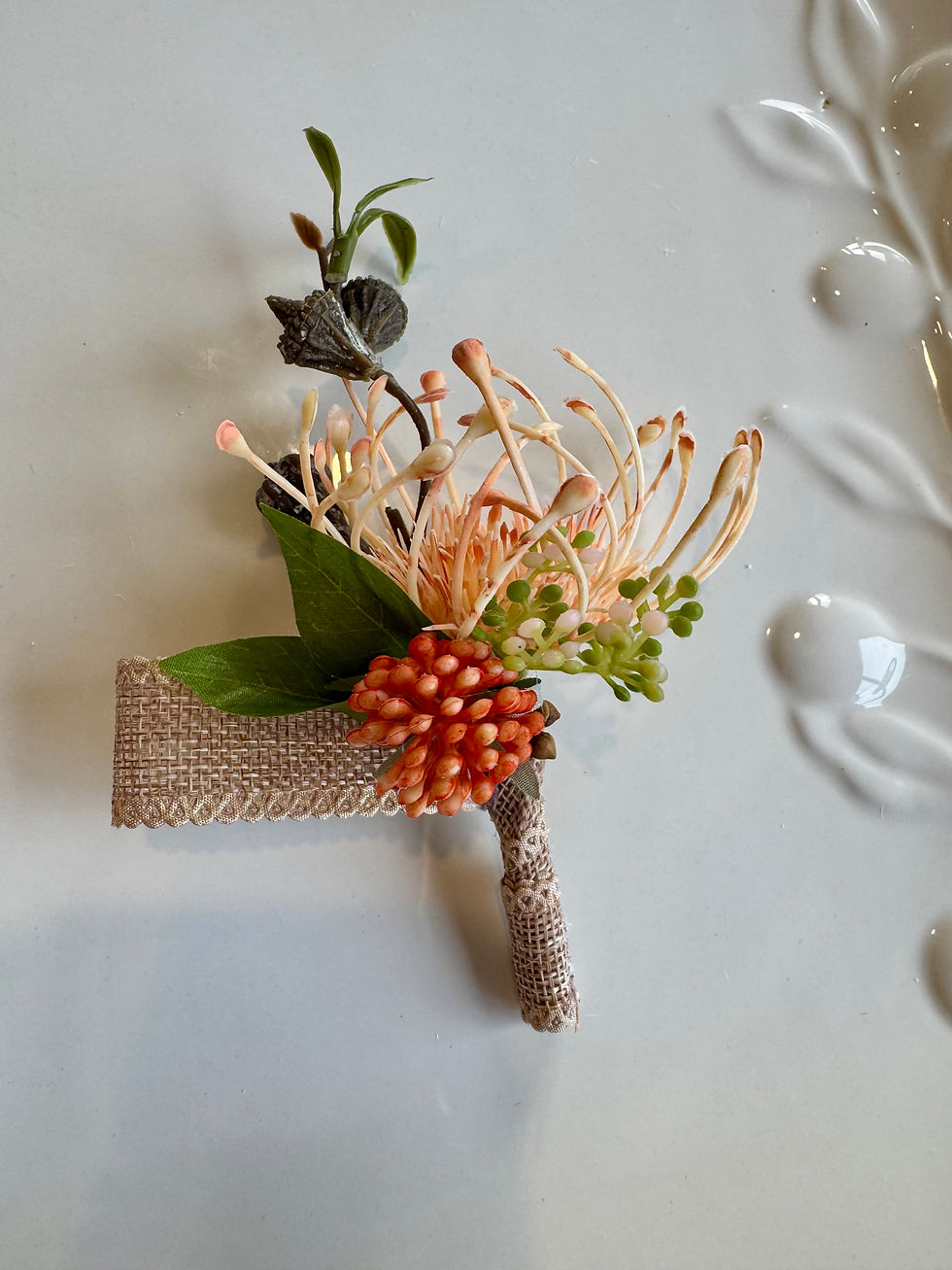 JW Weddings artificial floral buttonhole with tangerine buds, pincushion protea, brown burlap ribbon.