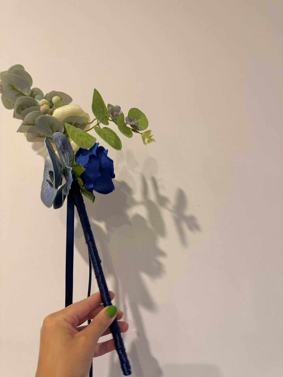 Wedding Flower Girl Wand ceremony accessory with blue rose, orchid and native eucalyptus. Held against white wall
