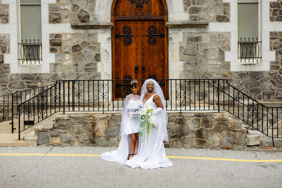 Bride outside beige stone church holding JW Weddings artificial cascade white orchid and rose bouquet next to flower girl.