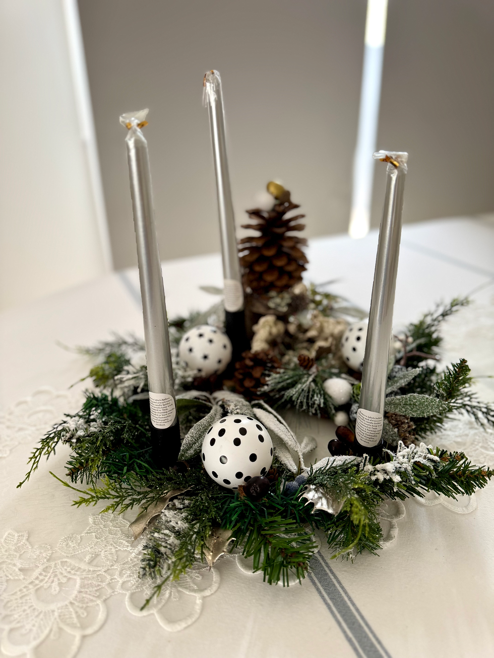 Top view of 3 pillar candle advent centrepiece with frosted green foliage, polka dot bauble, acorns and giant brown pinecone