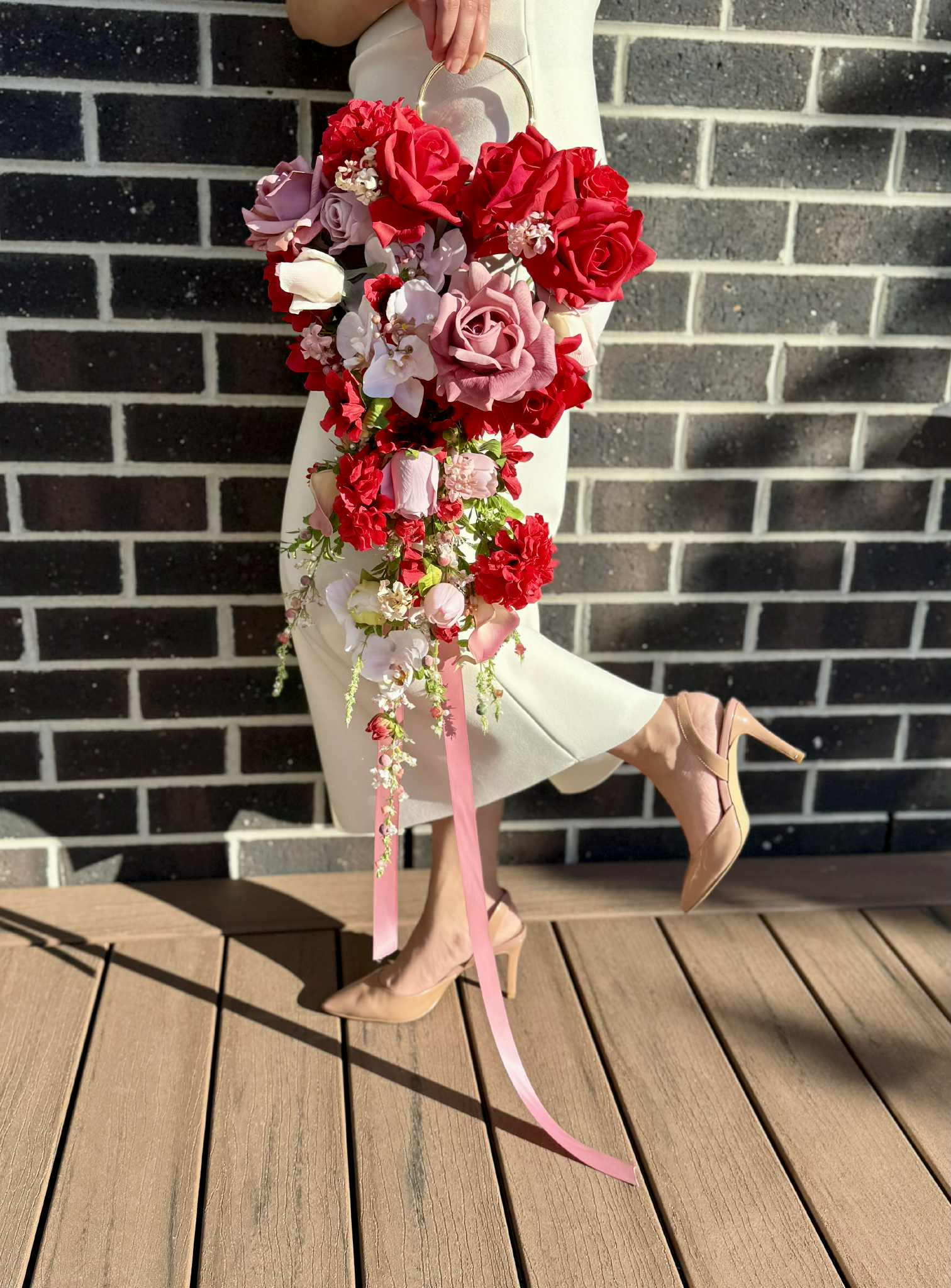 Bride holding a gold hoop cascading bridal bouquet with red roses, mauve roses, pink orchids, and trailing ribbons – luxury a