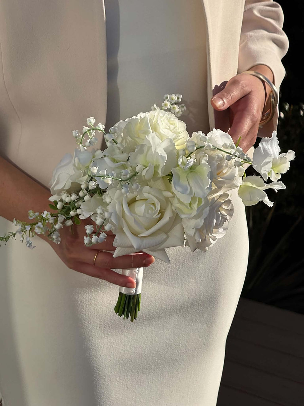 Bride in white dress and cashew colour capelet blazer holding petite white rose bouquet.