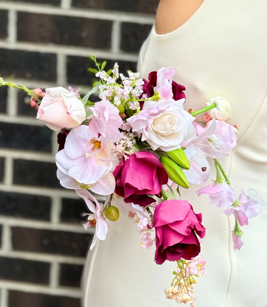 Thumbnail: Side view of free form maroon wedding bouquet with unstructured shape featuring orchid, rose, tulip, lily of valley