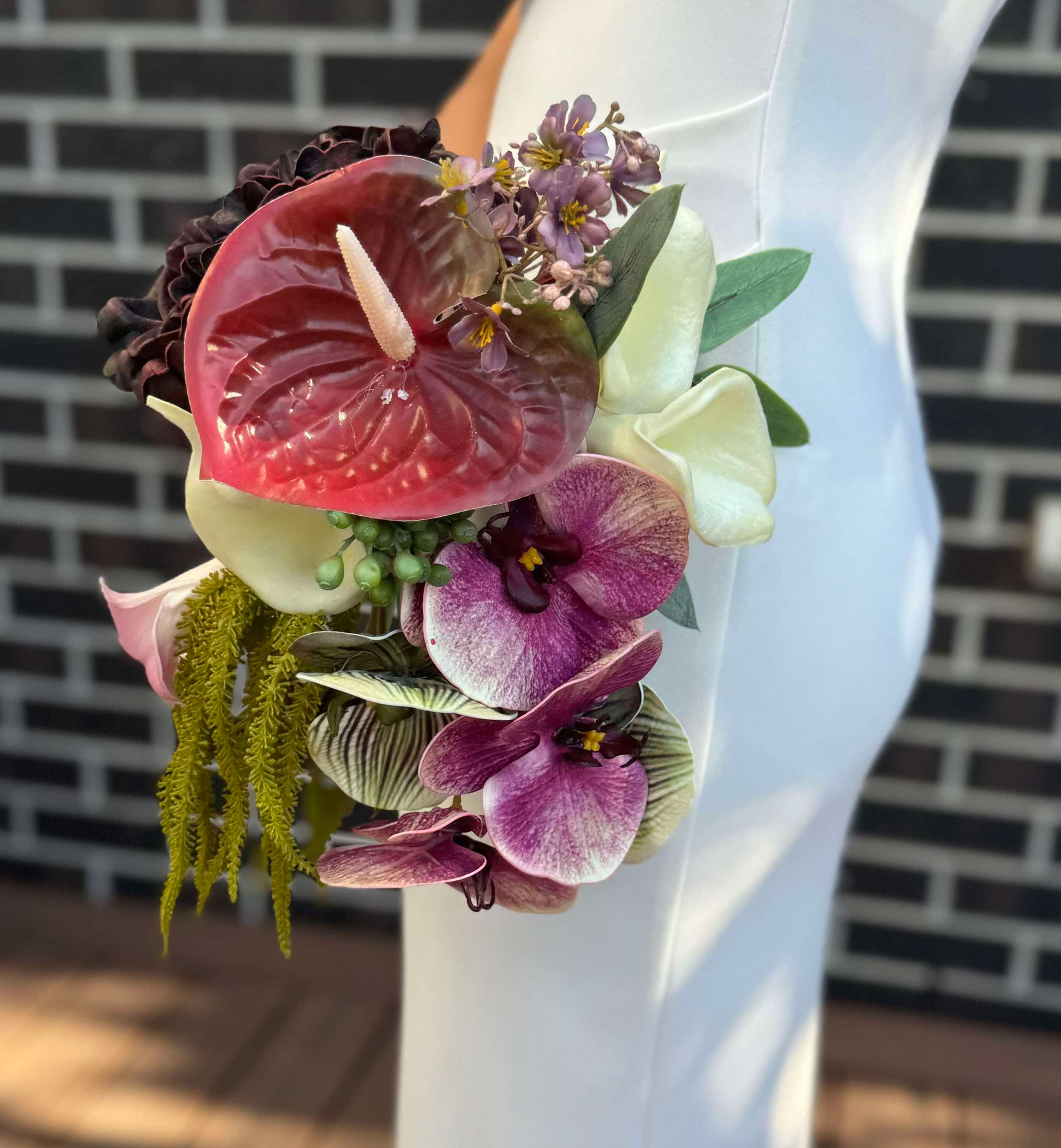 girl in white dress standing on her side holding bridal bouquet with red anthurium, amaranth, calla lily, orchid