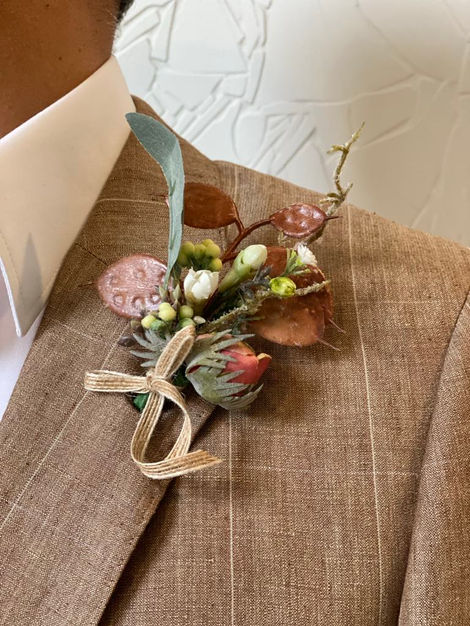 Man in sand beige oatmeal light brown tartan plaid suit wearing handmade boutonniere buttonhole with natural rustic looking elements like flat brown textured leaves, pink peony flower, tiny white flower buds.