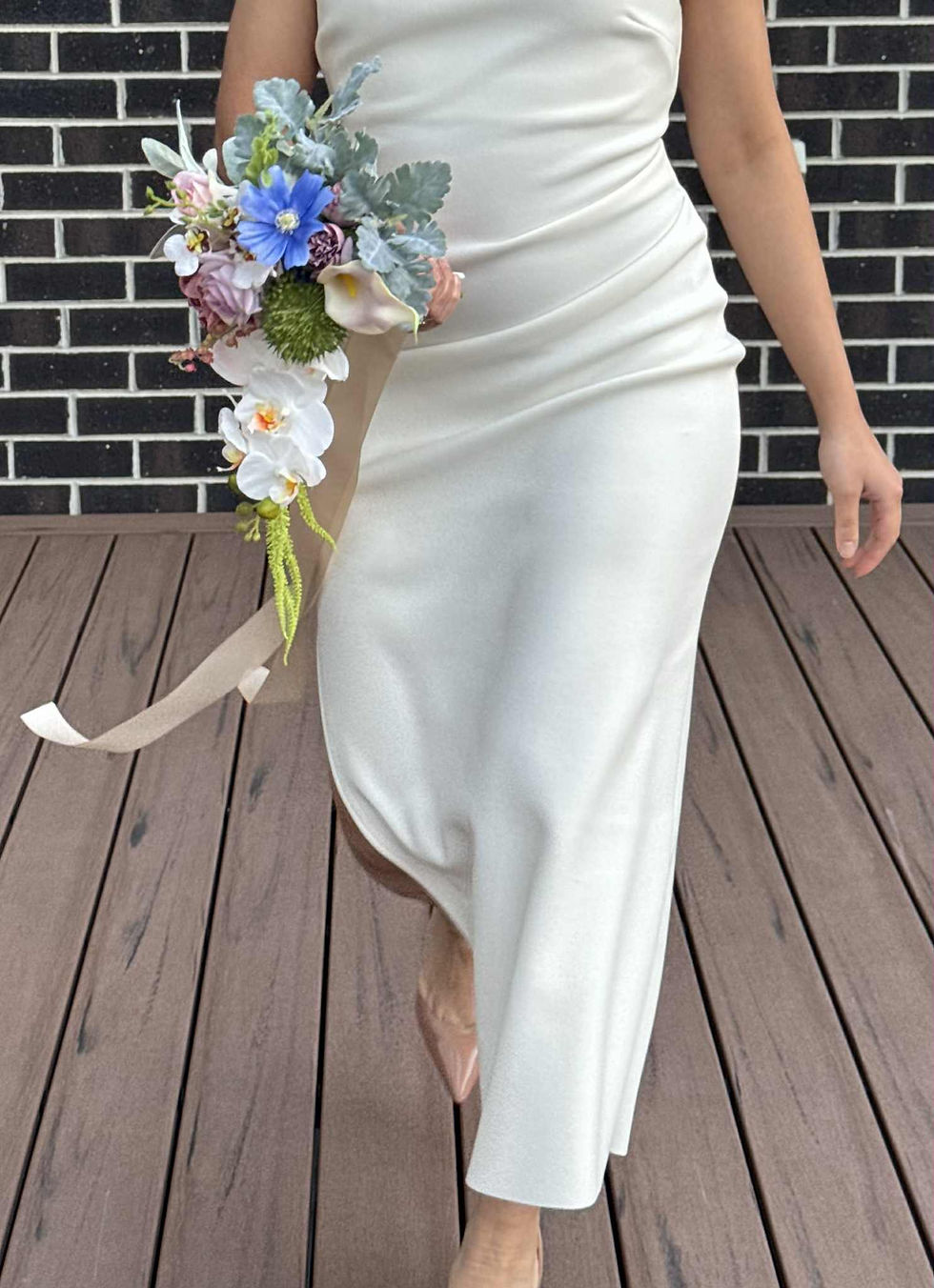 Thumbnail: Bride in white dress holding real touch artificial bridal bouquet with white orchid, blue cosmos, dusty pale pink roses.