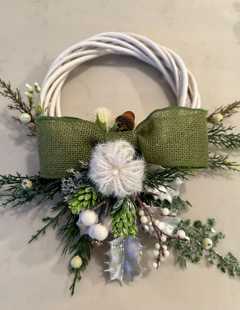 petite white Christmas wreath with large green burlap bow, white puff, and green foliage.