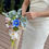 Thumbnail: Bride in white dress holding real touch artificial bridal bouquet with white orchid, blue cosmos, dusty pale pink roses.