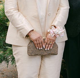 Lady in champagne silk suit holdin clutch and wearing JW Weddings artificial floral corsage with white peony and pink satin ribbon.