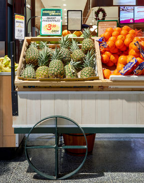 a display of pineapples and oranges in a grocery store - on a custom cart