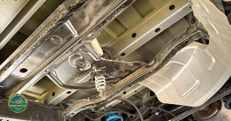 Underside of a vehicle showing suspension components with visible dirt. A logo on the left reads "Outdoor Adventure Muddy Ruttzz."